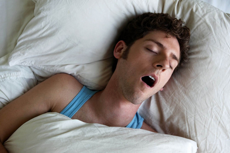 Man in a blue vest asleep with his mouth wide open