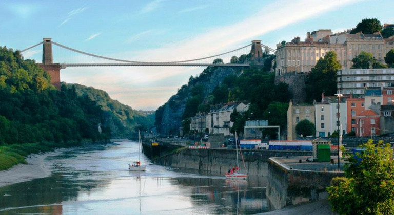 Sunset at Clifton Suspension Bridge, Bristol. Colourful houses to the side and two boats down the river