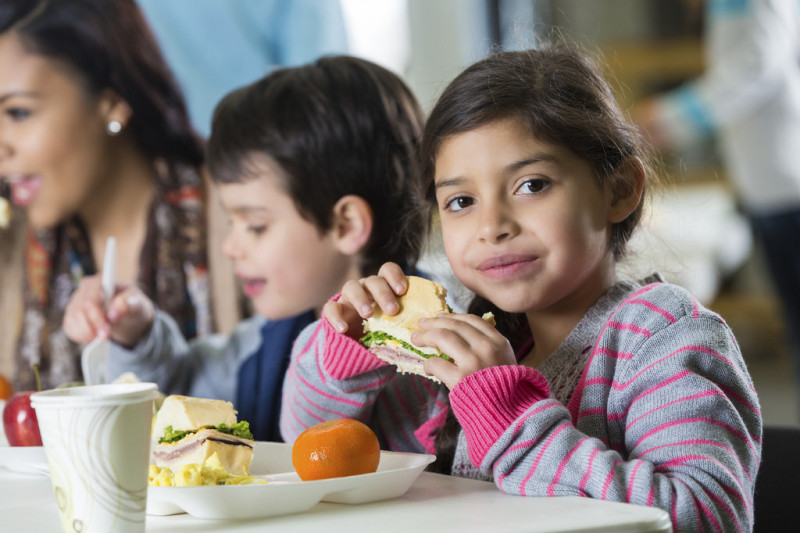 Young girl eating a sandwich with 2 people in the background