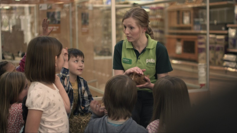 Pets At Home worker holding a guinea pig and talking to a group of children