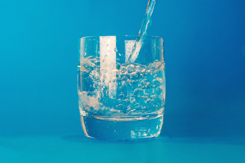 Water being poured into a glass tumbler on a blue background