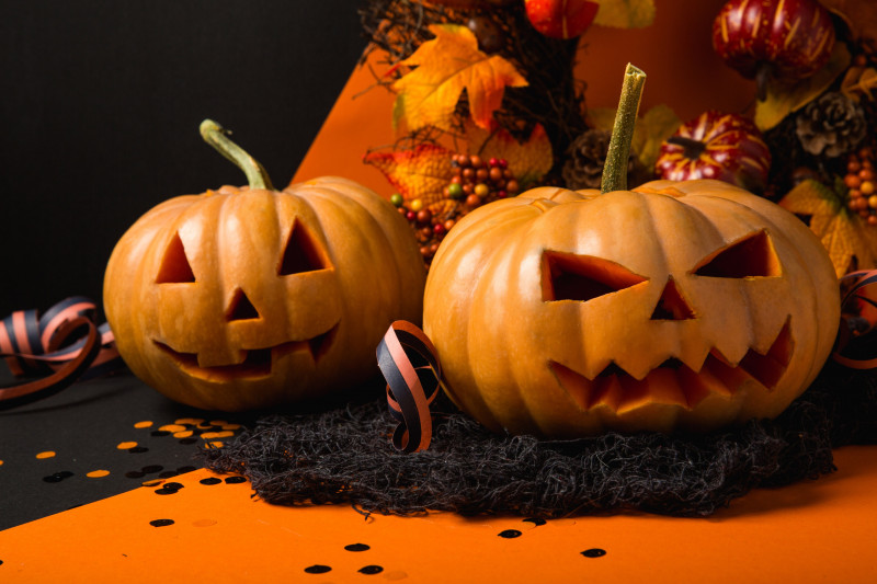 Two carved pumpkins on a black and orange table, adorned with Halloween decorations