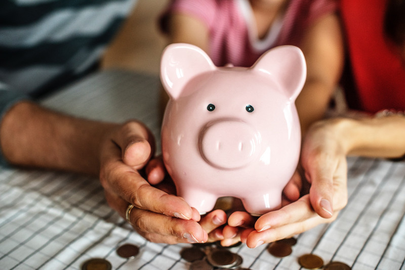 Two hands holding a pink Piggy Bank with coins out of focus below
