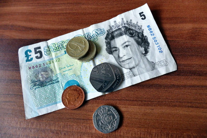 £5 note, 2x £1coin, 50p coin, 2p coin and 20p coin on a wooden background