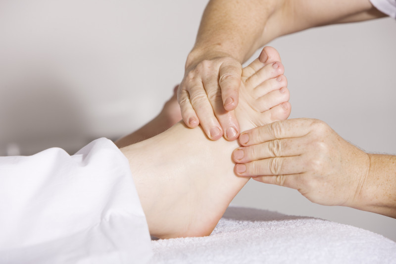 Close up of hand massaging foot wearing white trousers