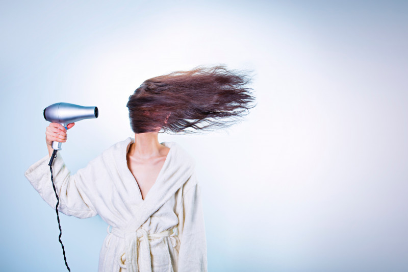 Brunette woman blow drying her hair wearing a dressing gown