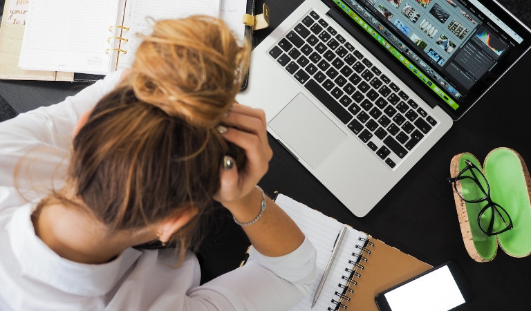 Birds eye image of woman sat at her laptop with her head in her hands
