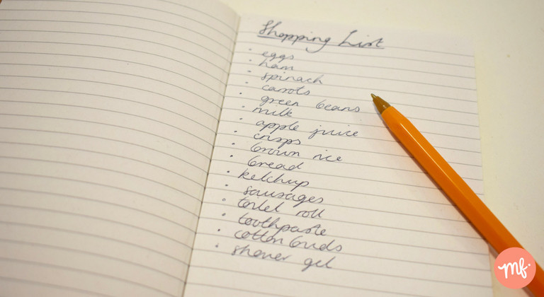 Lined notebook with shopping list written down, with yellow biro rested on top