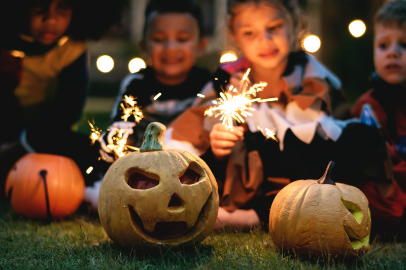 Carved pumpkins on the grass with children in the background playing with sparklers