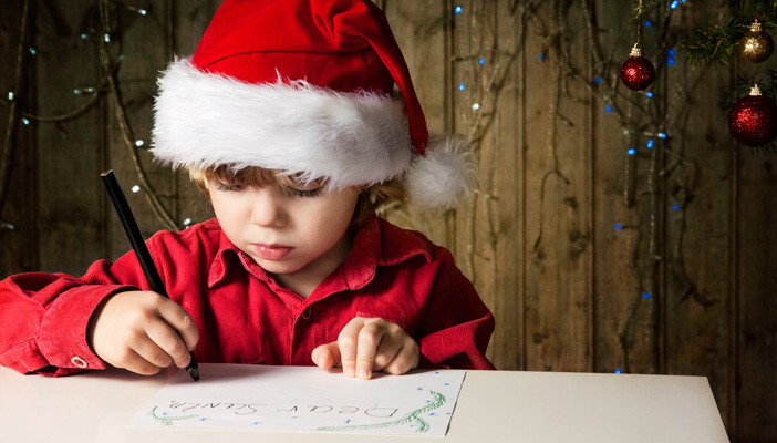 Young boy wearing Santa hat writing a letter to Santa