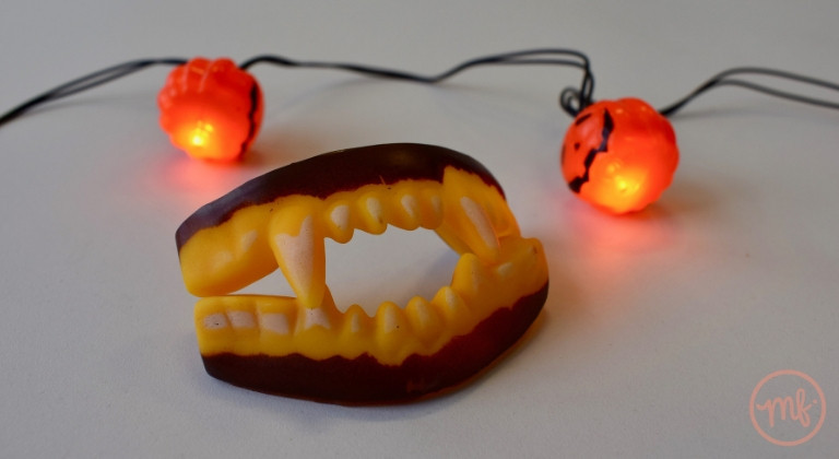 Close up of vampire teeth with pumpkin fairy lights in background
