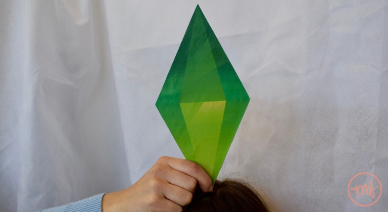 Hand holding a green Sim plumbob against a white background