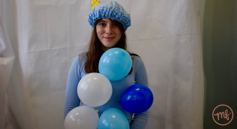 Woman with balloons stuck to body wearing a blue shower cap against a white background