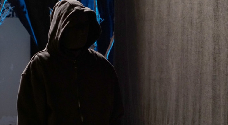 Figure stood in dark wearing black hoodie